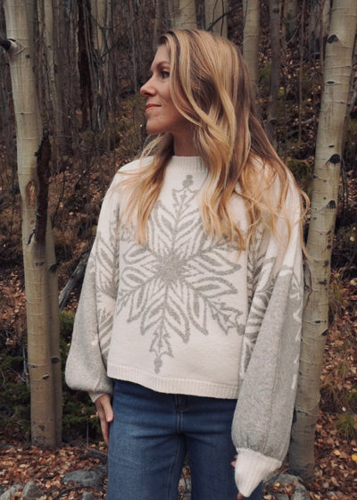 Woman wearing a patterned sweater standing in a forest with aspen trees.