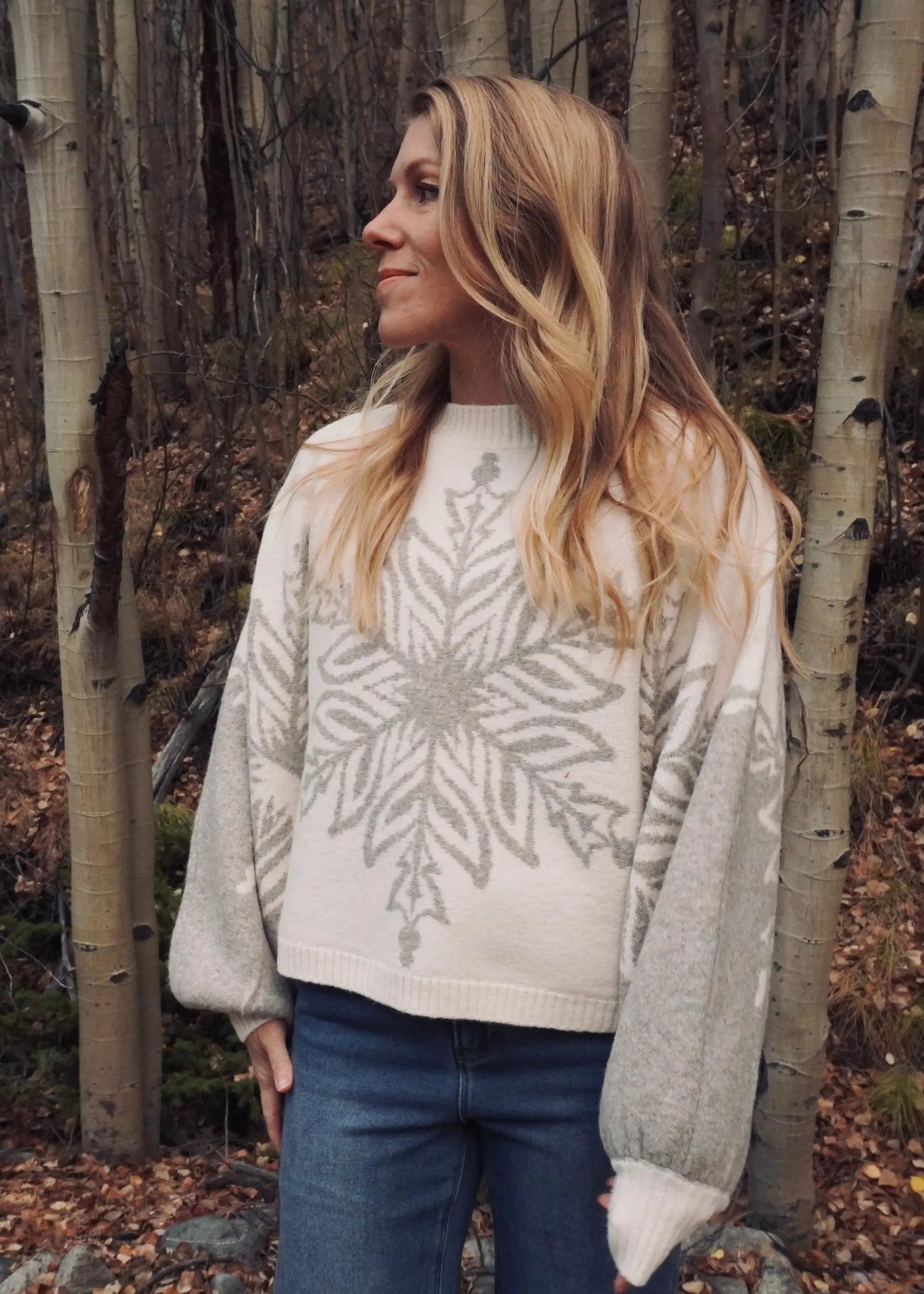 Woman wearing a patterned sweater standing in a forest with aspen trees.